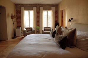 Ein Schlafzimmer mit einem großen Bett, zwei Sesseln, einem kleinen Tisch und einer Zimmerpflanze.