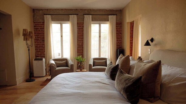 A bedroom with a large bed, two armchairs, a small table, and a potted plant.