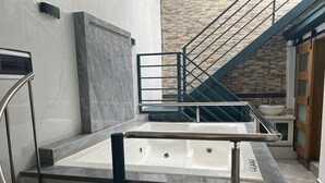 Un baño moderno con una bañera grande, una zona de ducha con mampara de vidrio y una escalera que lleva a un nivel superior.