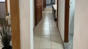 Un pasillo estrecho con puertas de madera y suelo de baldosas que conduce a una zona de cocina con un refrigerador y un lavamanos.