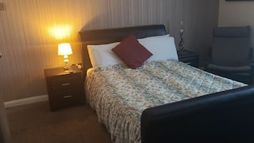 Una habitación de hotel con una cama, una mesita de noche con lámpara, una silla y una puerta.