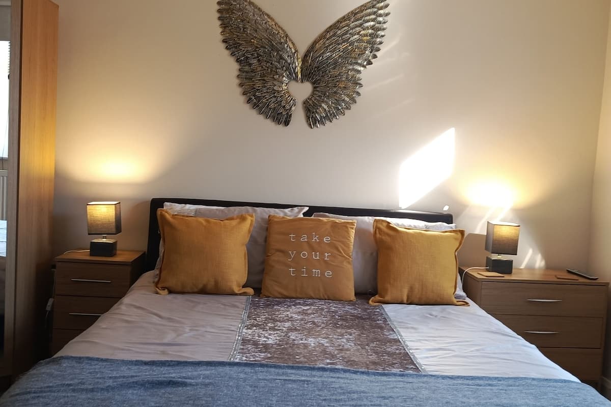 A bedroom with a bed, two bedside lamps, a wall-mounted decorative item, and a bedside table with a lamp.