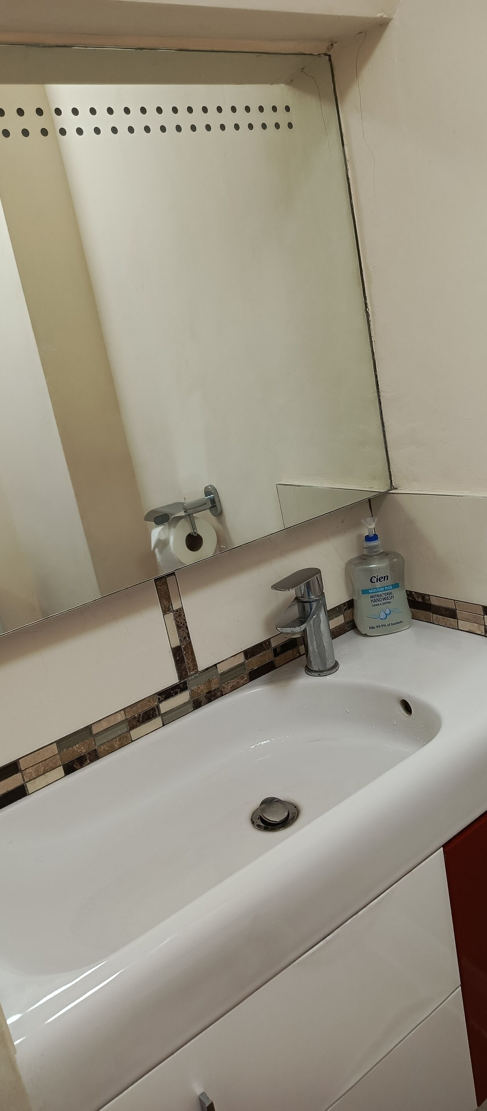 A bathroom with a white sink, a mirror, and a bottle of Cien hand soap.
