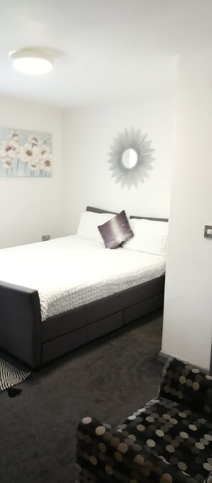 A bedroom with a bed, a wall-mounted mirror, and a floral painting. - New Accommodation  (Alfreton)