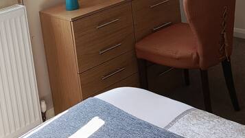 A bedroom with a wooden dresser, a mirror, a red chair, and a bed with a blue and white striped bedspread.