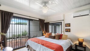 Hotelkamer met een bed, een plafondventilator, een airconditioner, een raam met gordijnen en uitzicht op het omliggende landschap.