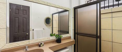 A bathroom with a beige sink, a mirror, a towel rack, a toilet, and a shower enclosure.