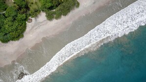 Luchtbeeld van een strand met helder turquoise water en een zandkust.