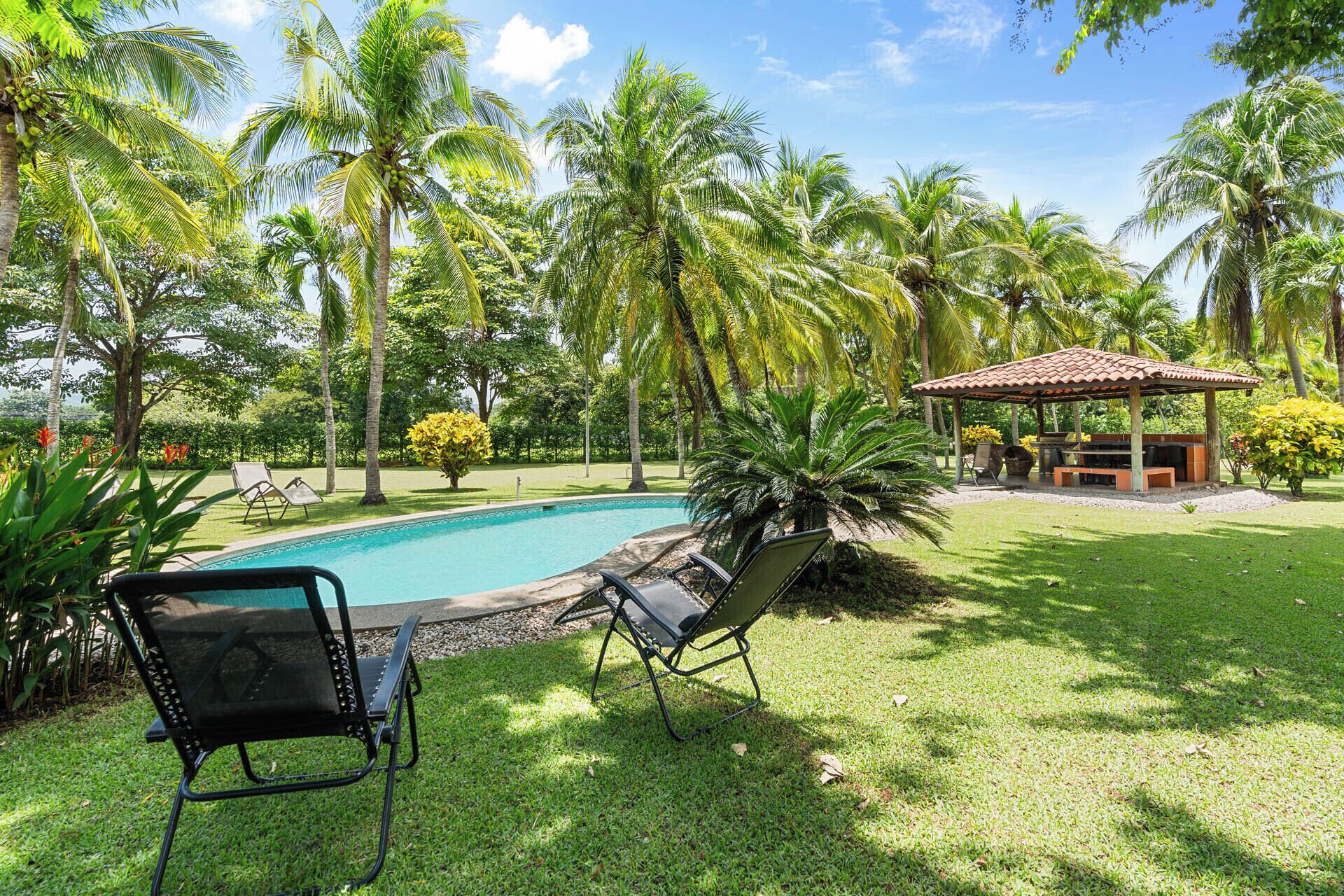 A poolside area with lounge chairs, a covered seating area, and lush greenery.