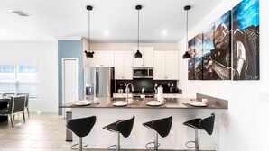 A modern kitchen with white cabinets, stainless steel appliances, and a central island with bar stools. - Last Minute Disney Getaway! Private Pool & Themed Bedrooms. Book Now! #87351 (Orlando)