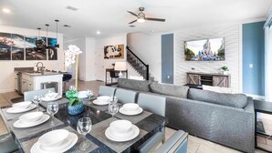 A modern living room with a dining table set for six, a grey sofa, and a staircase leading to another level. - Last Minute Disney Getaway! Private Pool & Themed Bedrooms. Book Now! #87351 (Orlando)
