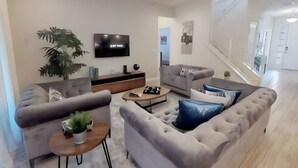 A modern living room with a grey sofa, a coffee table, and a TV on the wall. - Last Minute Disney! Private Pool, Hot Tub, Game Room & Themed Bedrooms. Book Now! #113319 (Orlando)