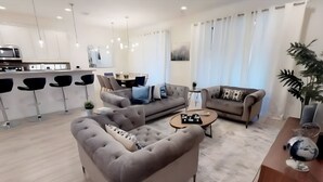 A modern living room with a grey sofa, a smaller sofa, and a coffee table. There is a dining area with a table and chairs in the background. - Last Minute Disney! Private Pool, Hot Tub, Game Room & Themed Bedrooms. Book Now! #113319 (Orlando)