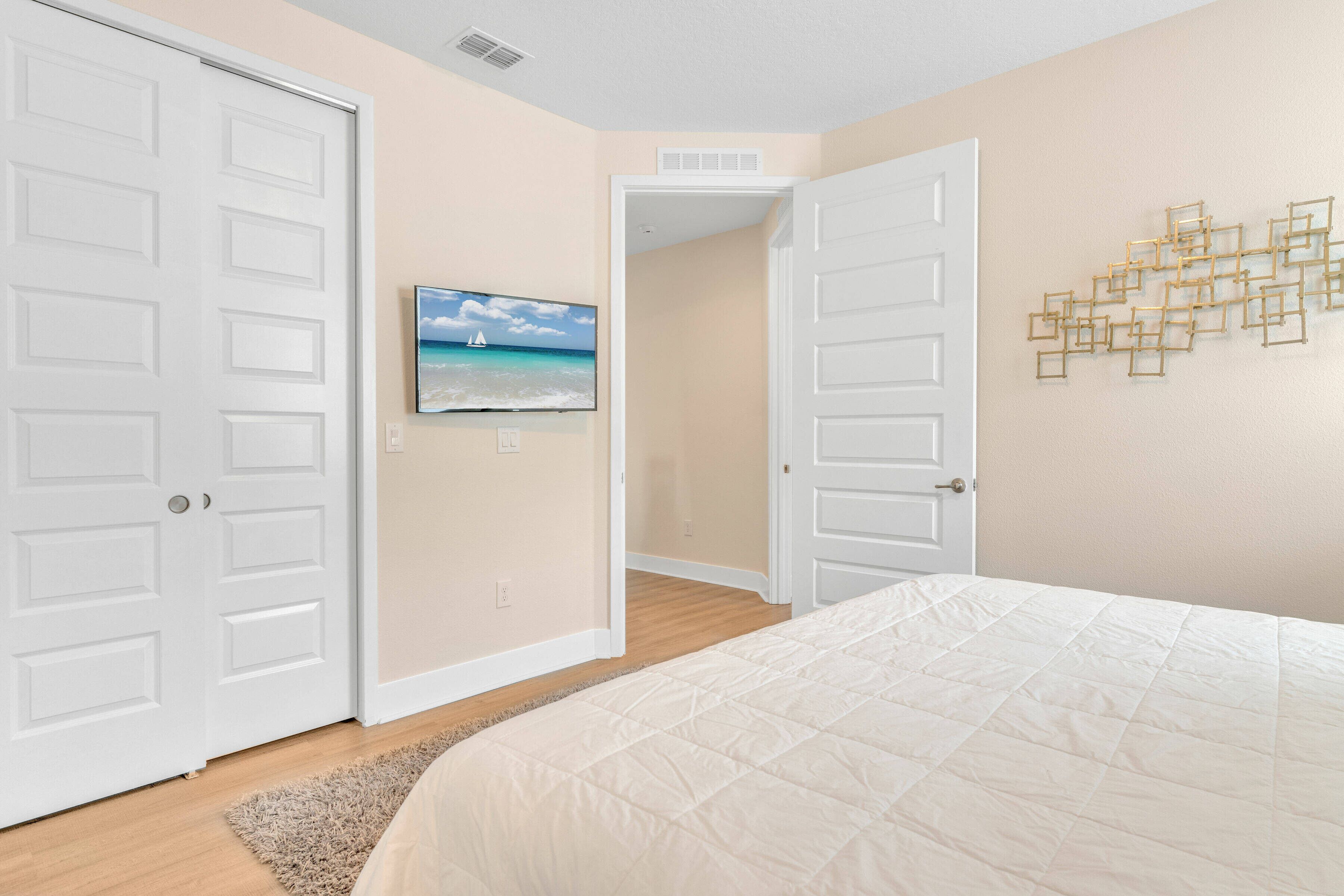 A bedroom with a bed, two white doors, a wall-mounted TV, and a decorative wall piece.