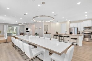 Uma cozinha moderna com uma ilha grande, banquetas brancas, eletrodomésticos de aço inoxidável e iluminação embutida.
