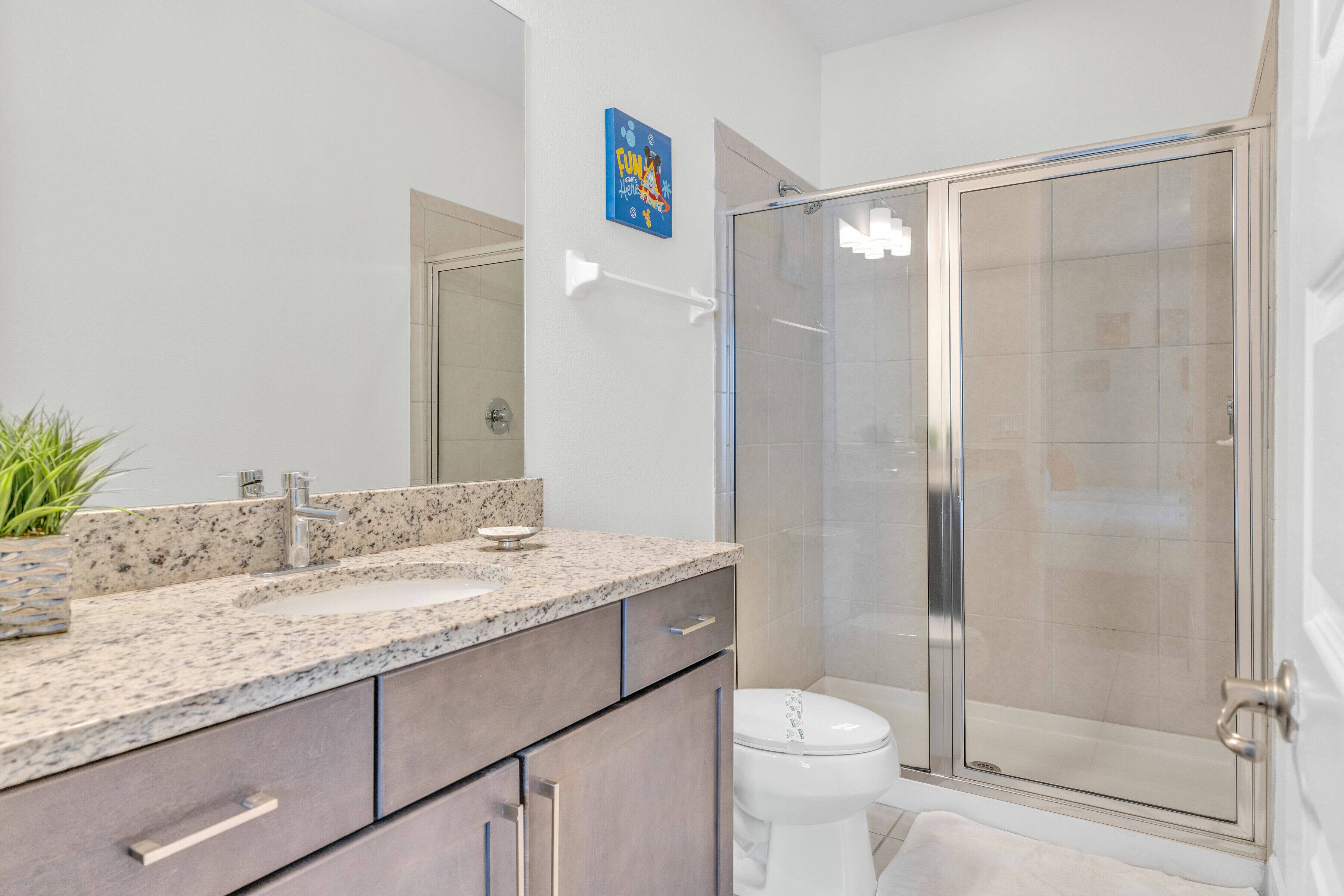 A modern bathroom with a granite countertop, two sinks, a toilet, and a glass-enclosed shower.