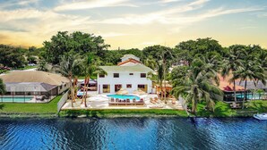 A large white house with a swimming pool, surrounded by palm trees and a body of water. - Tulum Villa (Pembroke Pines)