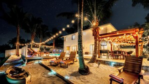 A beachfront property with a pool, lounge chairs, and string lights. - Tulum Villa (Pembroke Pines)