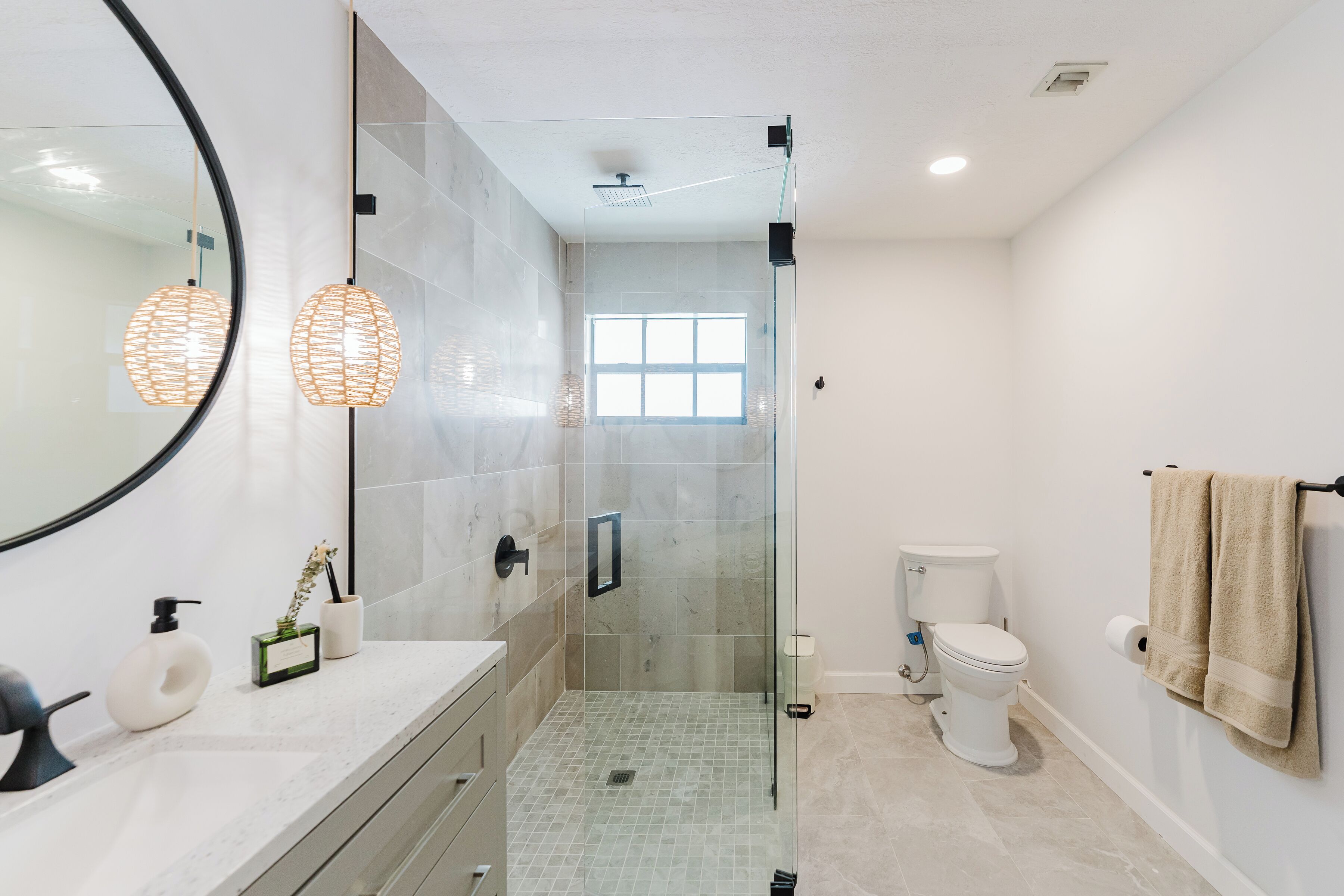 A modern bathroom with a glass-enclosed shower, a large mirror, and a toilet with a towel rack.