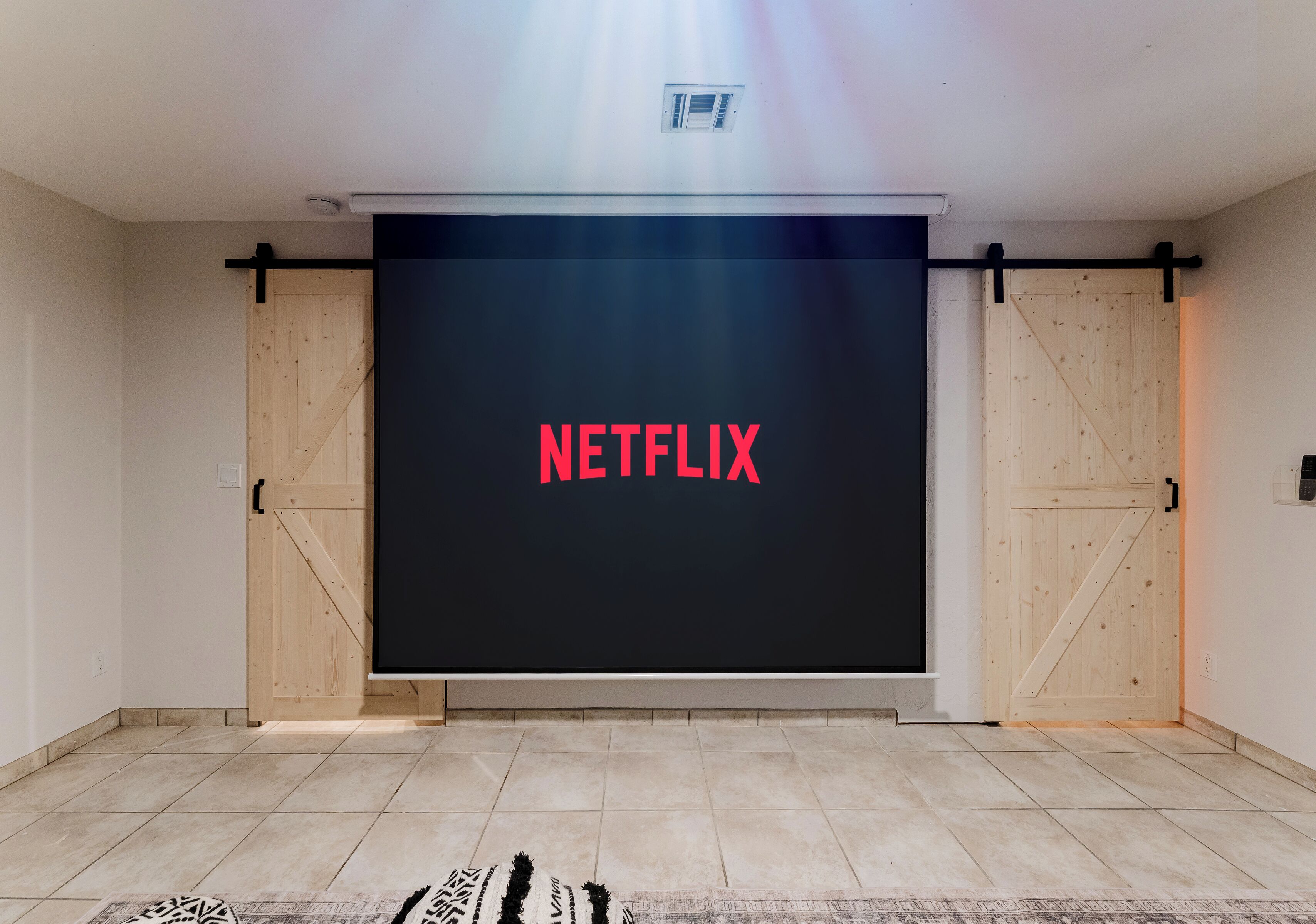 A room with a large screen displaying the Netflix logo, wooden sliding doors, and a patterned rug on the floor.