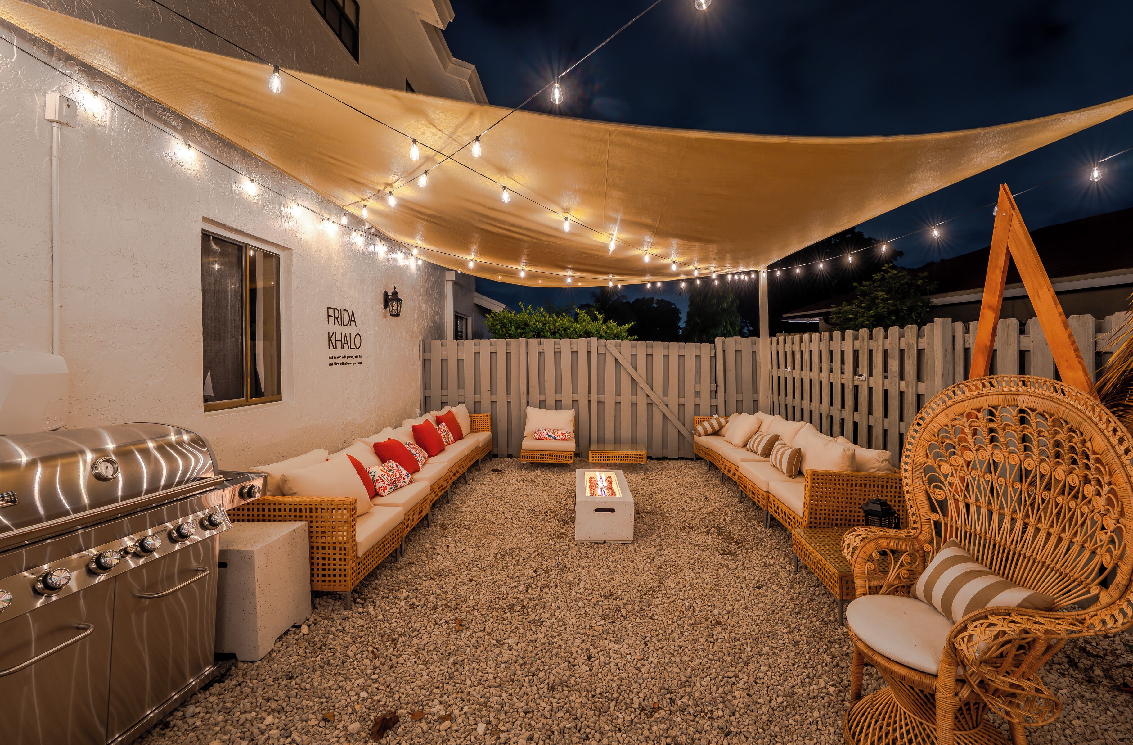 Un patio al aire libre con una parrilla, muebles de mimbre y luces colgantes.