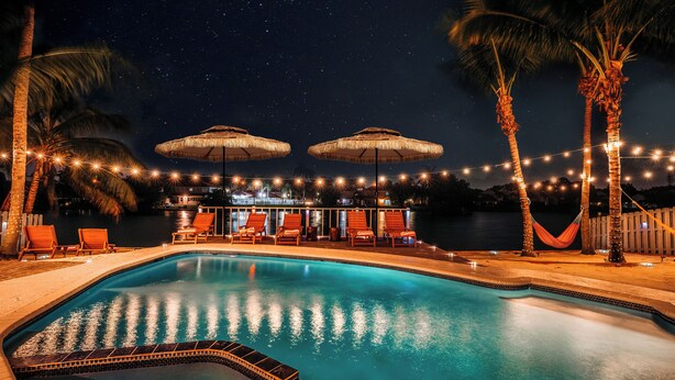 A nighttime pool area with string lights, palm trees, and umbrellas. - Tulum Villa (Pembroke Pines)