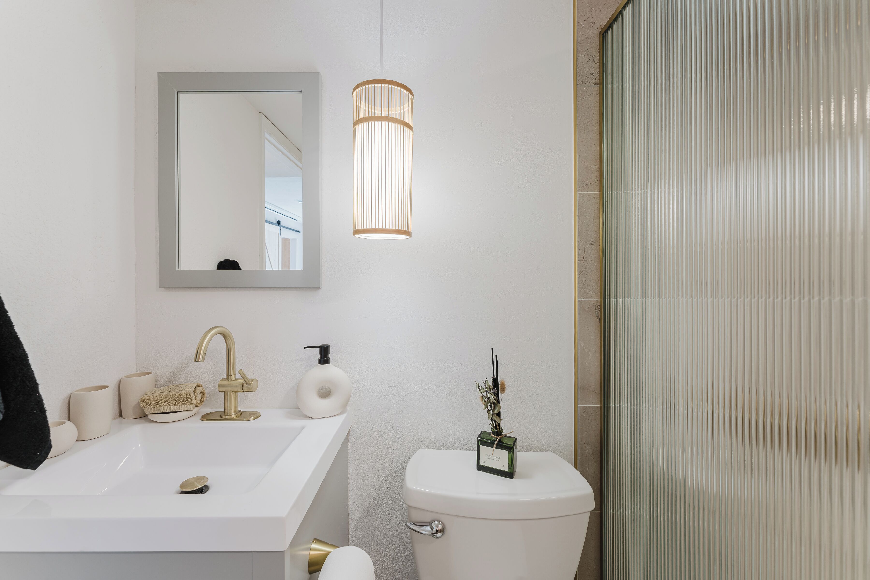 A bathroom with a white sink, gold faucet, and toilet. There is a mirror above the sink and a light fixture above the toilet.