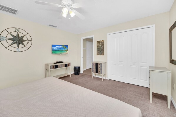 A bedroom with a bed, a ceiling fan, a painting, a wardrobe, and a small table.