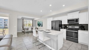 A modern kitchen with white cabinetry, stainless steel appliances, and a central island with bar stools.