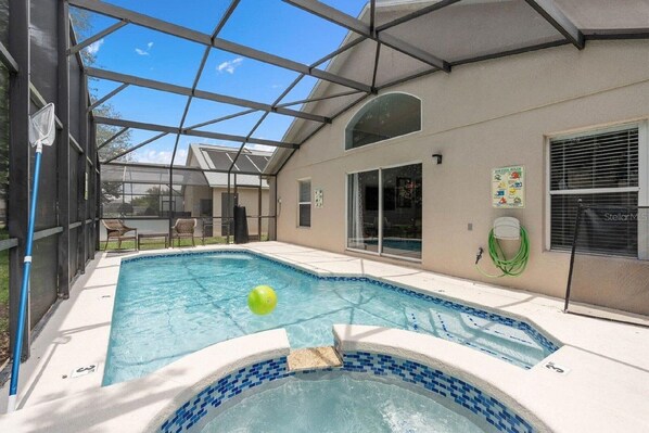 Piscina con cerramiento de vidrio, jacuzzi y zona de patio techada.