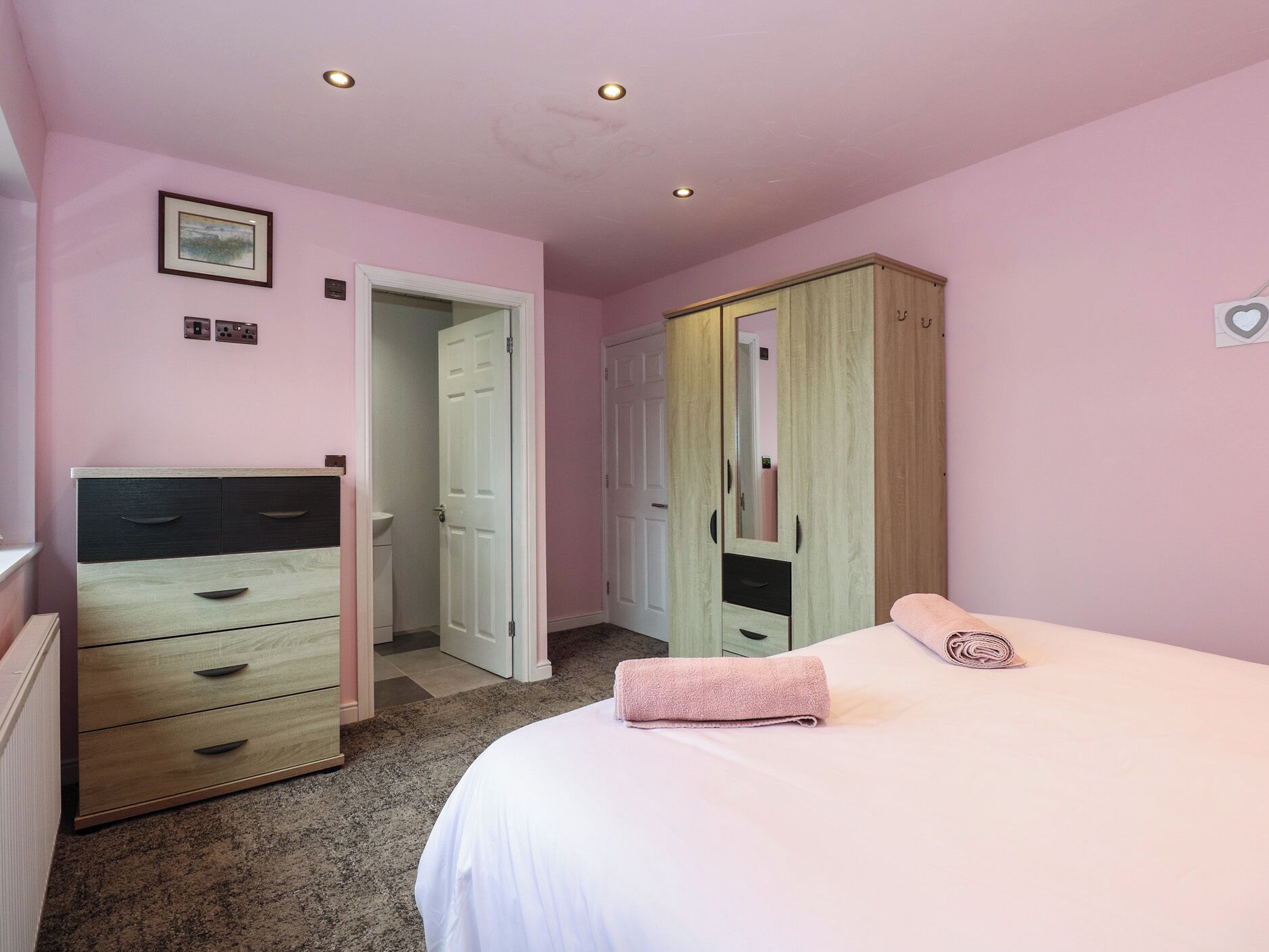 Une chambre à coucher comprenant un lit, une armoire en bois, une commode et une porte donnant accès à une salle de bain.
