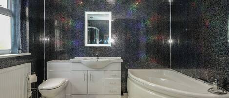 A modern bathroom with a black speckled wall, a white sink, a toilet, and a freestanding bathtub.