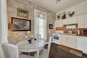 A dining area with a round glass table, white chairs, and a white cabinet with a stove. - Two Suite Getaway with Balcony overlooking Main St (Fredericksburg)