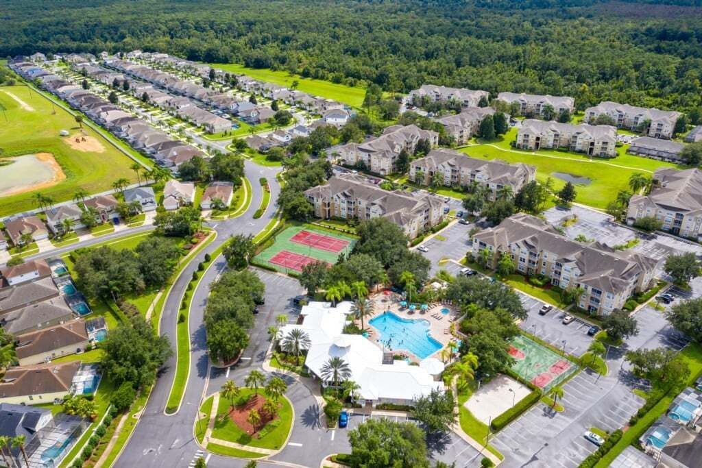 An aerial view of a residential area with apartment buildings, a swimming pool, tennis courts, and green spaces.