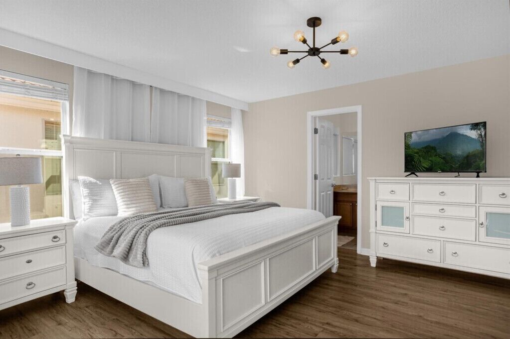 A bedroom with a large bed, a white dresser, a television, and a chandelier.