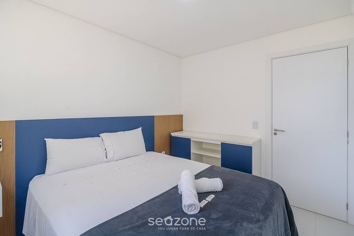 A hotel room with a bed, a nightstand, a door, and a wall unit.