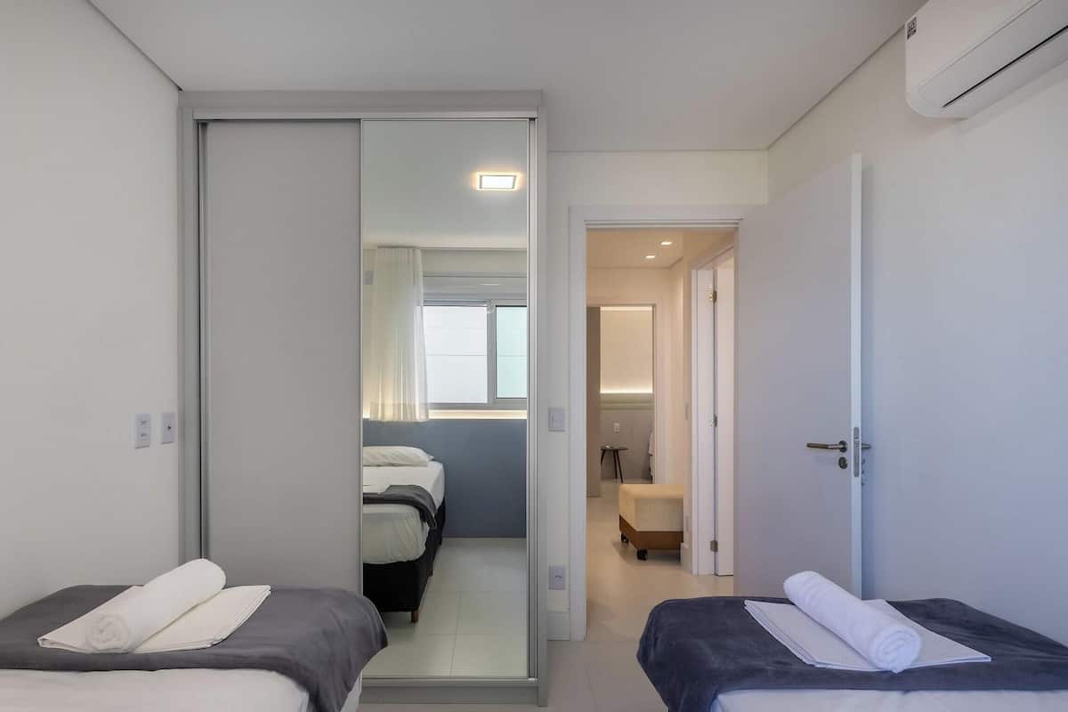 A modern hotel room with two beds, a sliding door leading to a bathroom, and an air conditioning unit on the wall.
