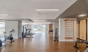 Un gimnasio con equipo de ejercicio, una escalera de madera y vistas de edificios a través de amplios ventanales.