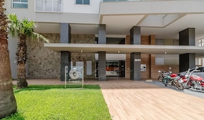Un edificio moderno con fachada de piedra, un acceso cubierto y un estacionamiento con motocicletas.