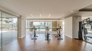 A gym with exercise equipment, large windows, and a view of buildings. - Seafront Condominium With Pool - SHC (Picarras)