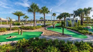 Ein Golfplatz mit mehreren grünen Rasenflächen, Palmen und blauem Himmel.
