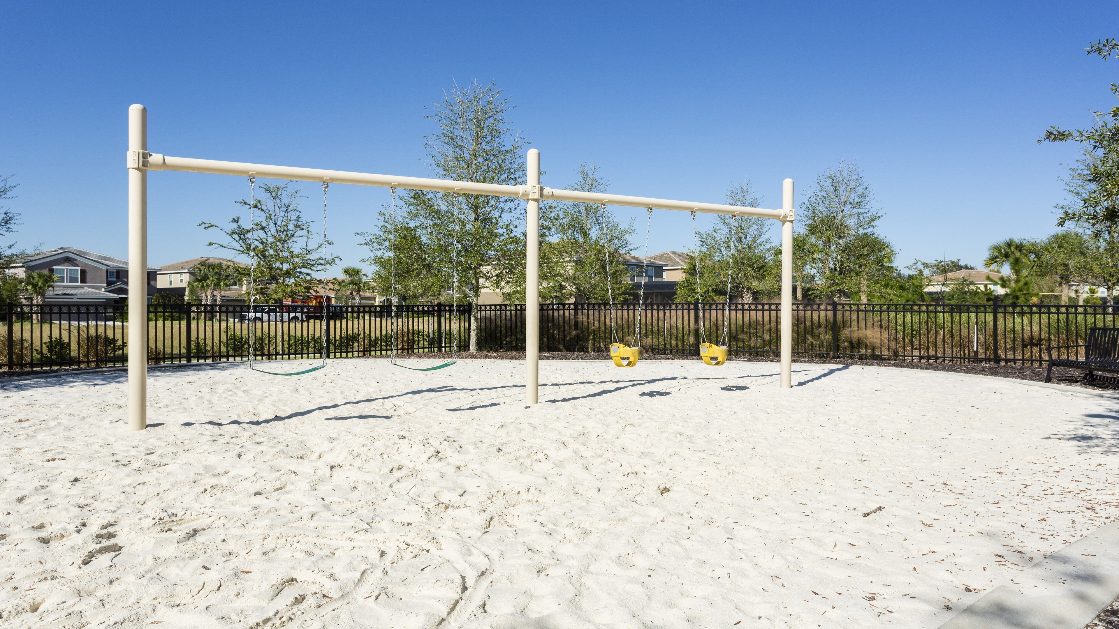A playground with swings and a sandpit, surrounded by a fence and trees.