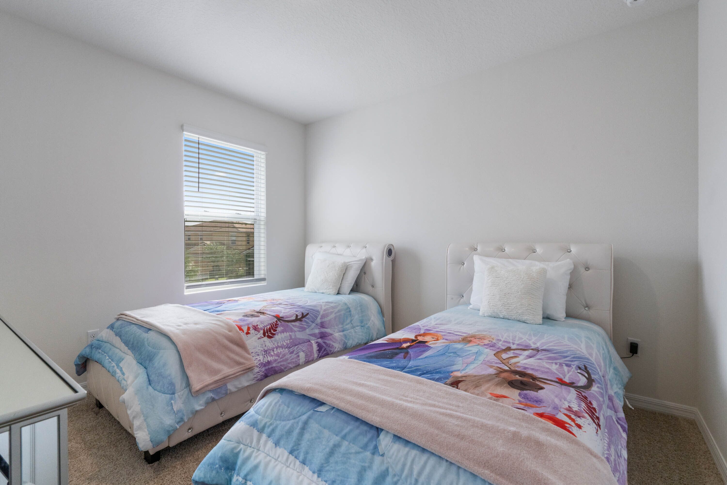 A bedroom with two beds, each with a headboard, a window with blinds, and a carpeted floor.