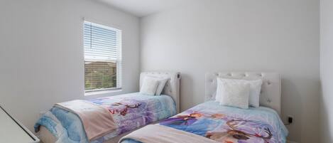 A bedroom with two beds, each with a headboard, a window with blinds, and a carpeted floor.