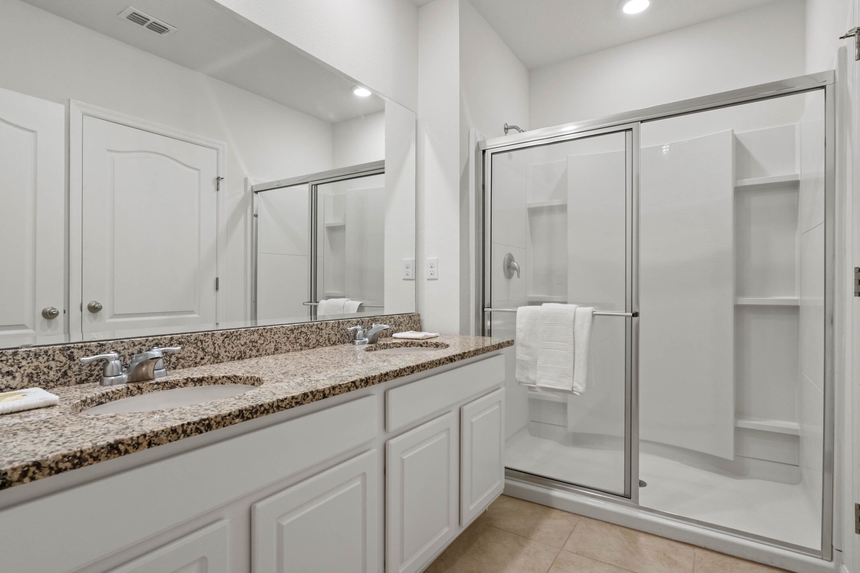 A modern bathroom with a granite countertop sink, white cabinets, a large mirror, and a glass-enclosed shower.