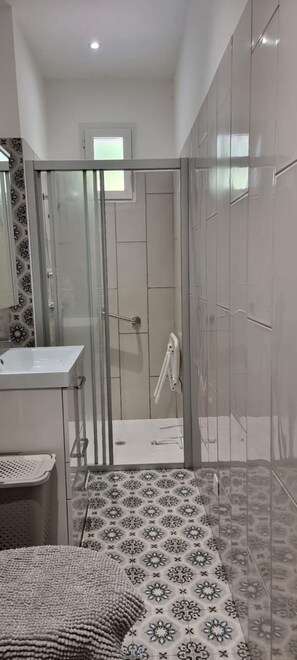 Ein modernes Badezimmer mit einer Duschkabine aus Glas, einem weißen Waschbecken und Fliesen mit Muster.