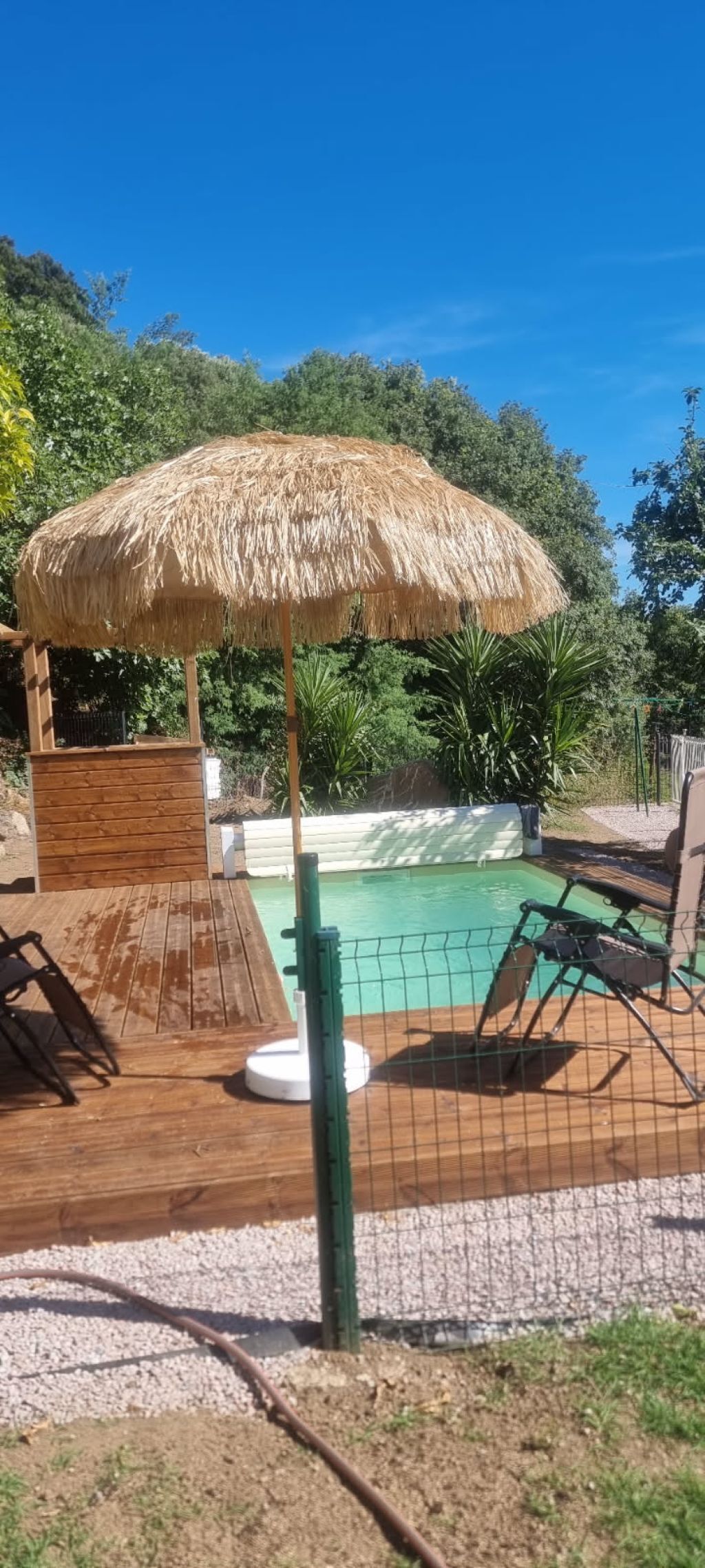 Uma área de piscina com deck de madeira, guarda-sol de palha e piscina cercada.