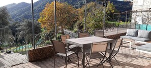Eine Außenterrasse mit Tisch, Stühlen und einer Sitzecke, mit Blick auf eine gebirgige Landschaft.