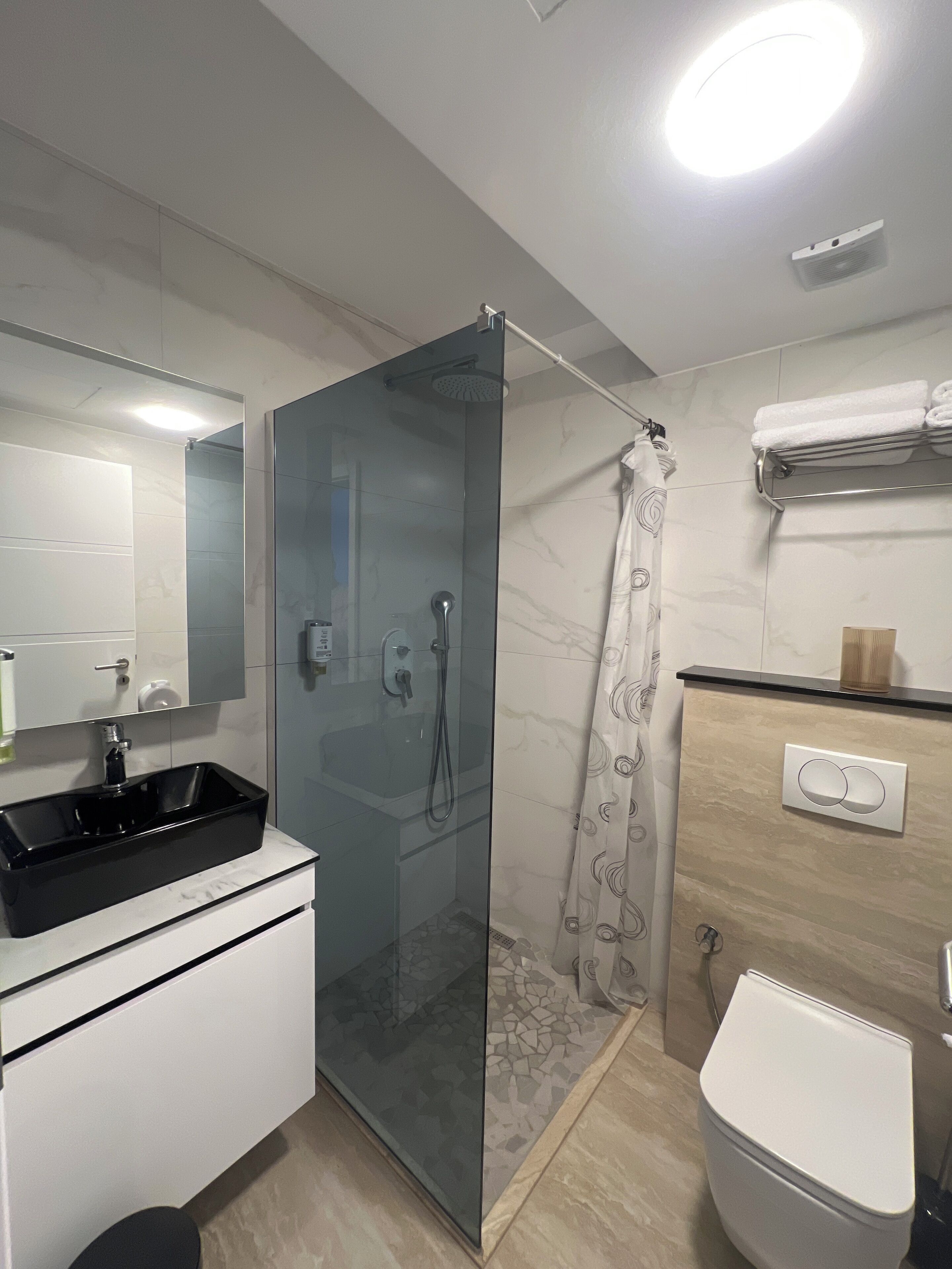 Ein modernes Badezimmer mit einer Duschkabine, einem schwarzen Waschbecken und einer weißen Toilette.