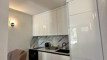 A compact kitchen with white cabinets, a marble backsplash, and a black countertop.